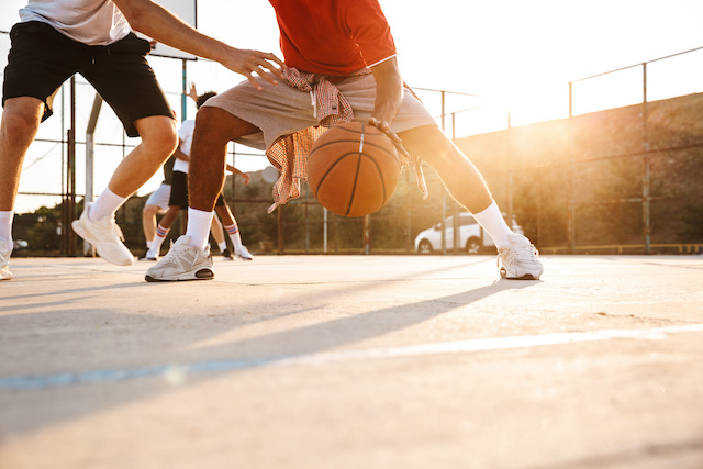 En man i grå shorts och en röd skjorta dribblar en basketboll.